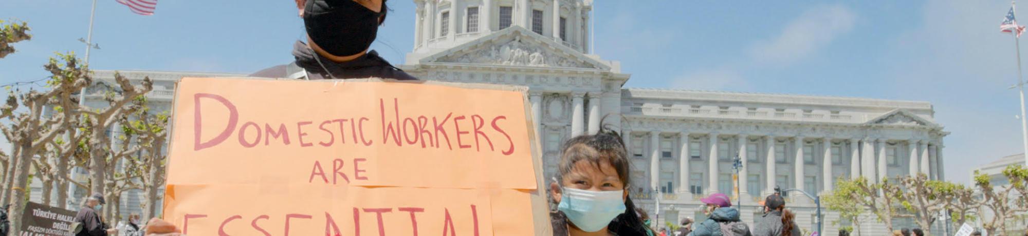 Mjer mostrando un cartel que dice que los trabajadores domesticos son esenciales